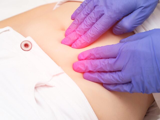 image of a doctor's gloved hands pressing on a woman's stomach